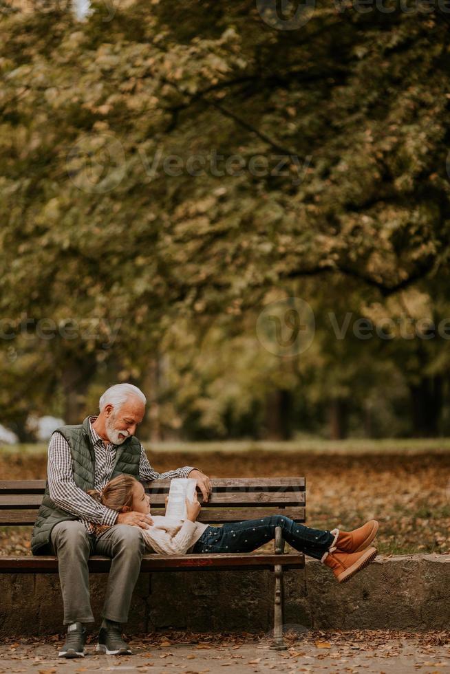 Großvater verbringt am Herbsttag Zeit mit seiner Enkelin auf der Bank im Park foto