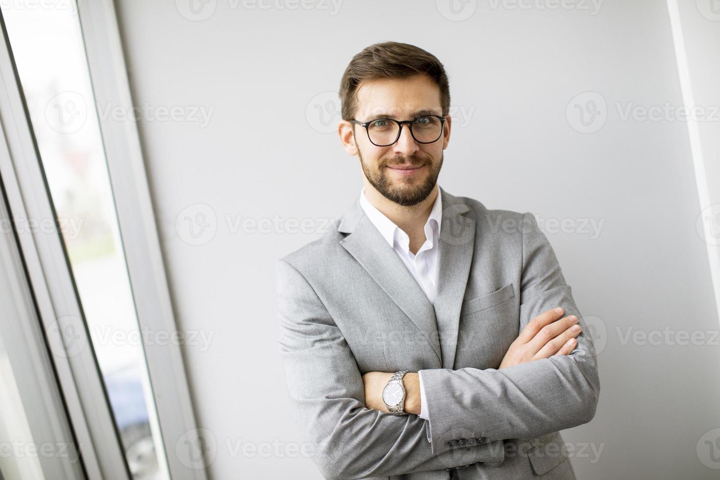 Junger moderner Geschäftsmann, der im Büro an der Wand steht foto