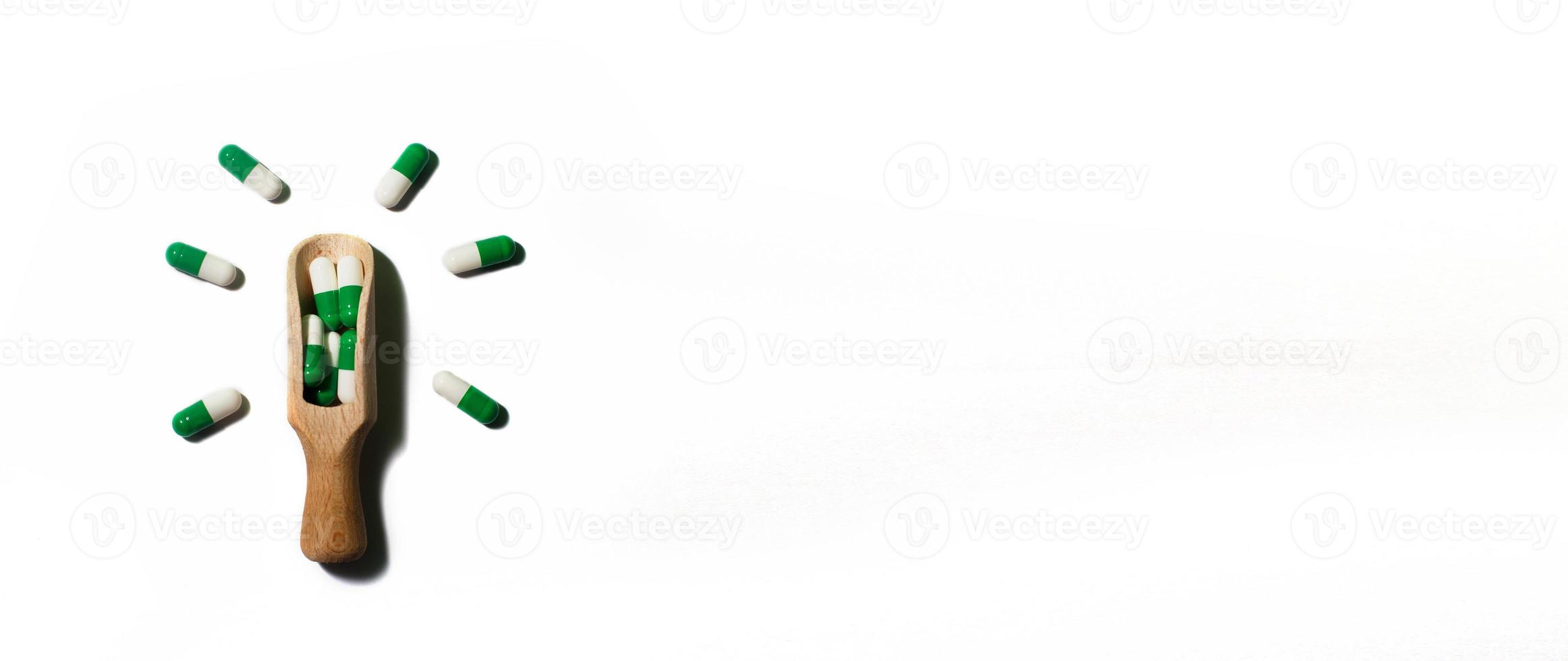 Medizin grüne Pillen auf weißem Hintergrund auf einem Holzlöffel in Form einer Glühbirne. Platz für Text kopieren. Banner foto