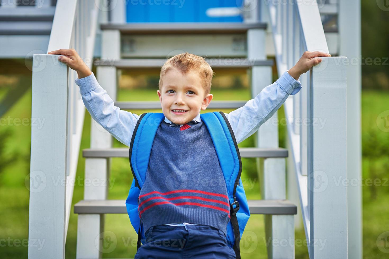 glücklicher kleiner vorschulkindjunge mit rucksack, der draußen aufwirft foto