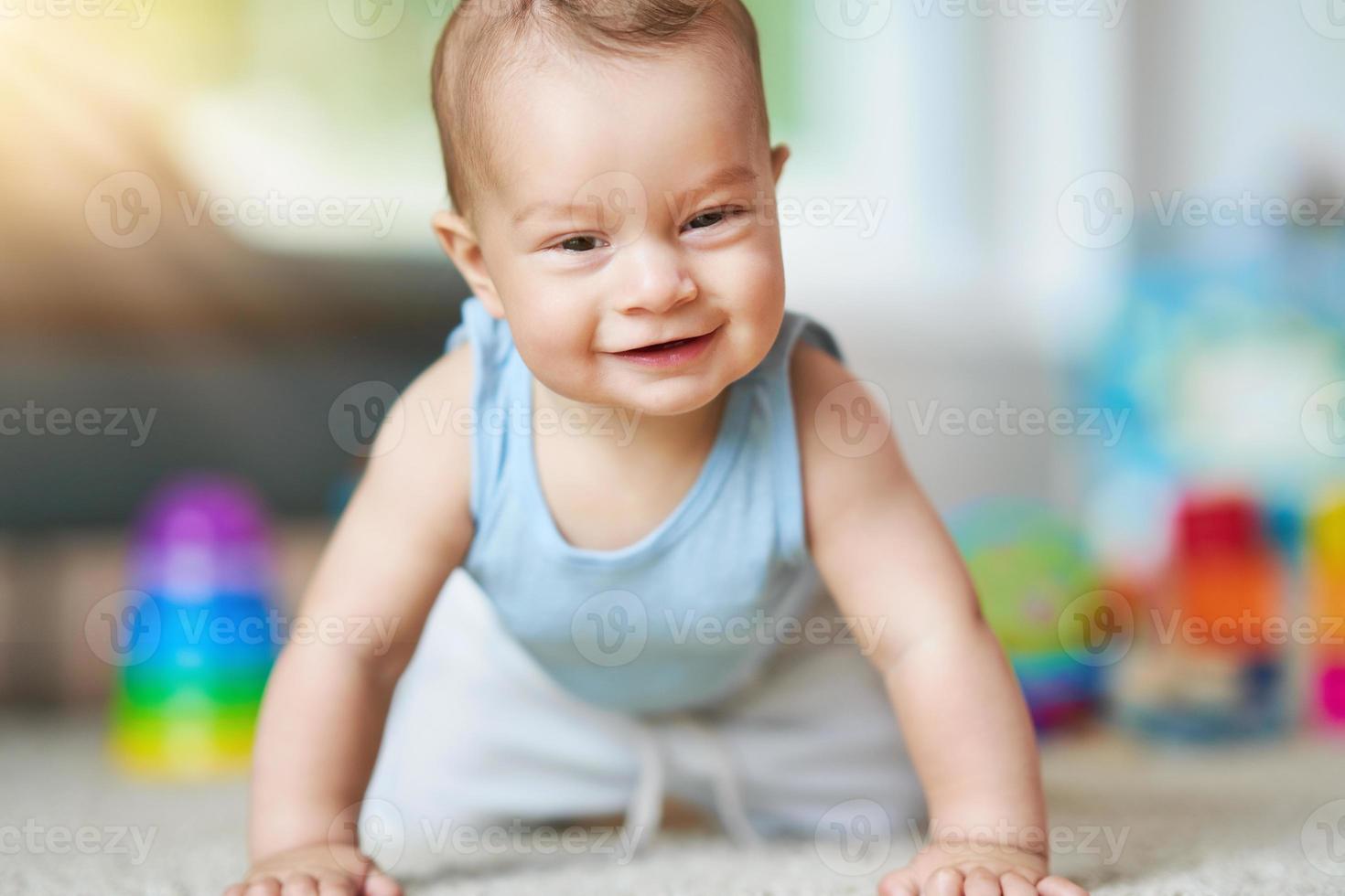 süßer lächelnder kleiner Junge, der im Wohnzimmer auf dem Boden krabbelt foto
