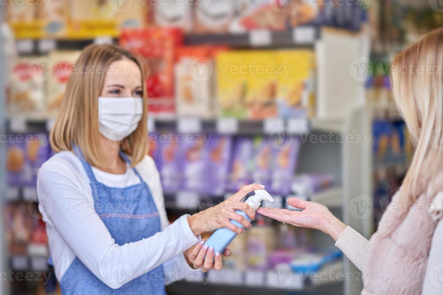 erwachsene frau in medizinischer maske mit handdesinfektionsmittel vor dem einkauf von lebensmitteln foto