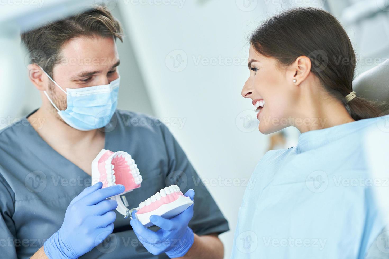 männlicher zahnarzt, der frau in der zahnarztpraxis kiefer zeigt foto