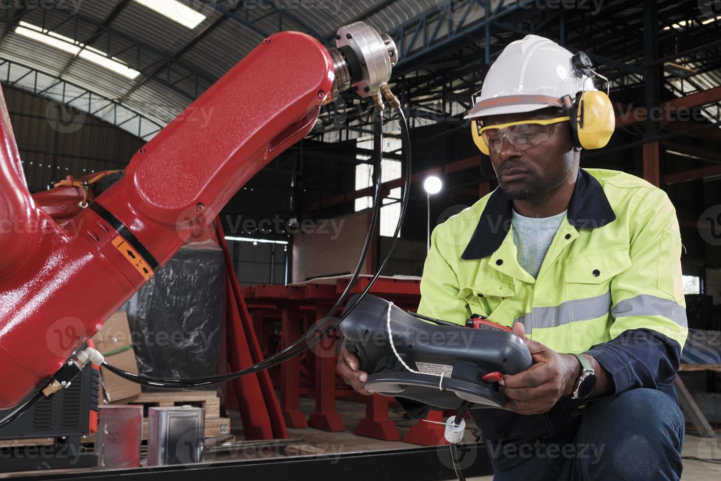 Ein afroamerikanischer Produktionsingenieur testet und steuert Roboterarme in einer mechanischen Fertigungsfabrik, intelligente automatische Maschinen im Industriegeschäft und futuristische Technologieinnovationen. foto