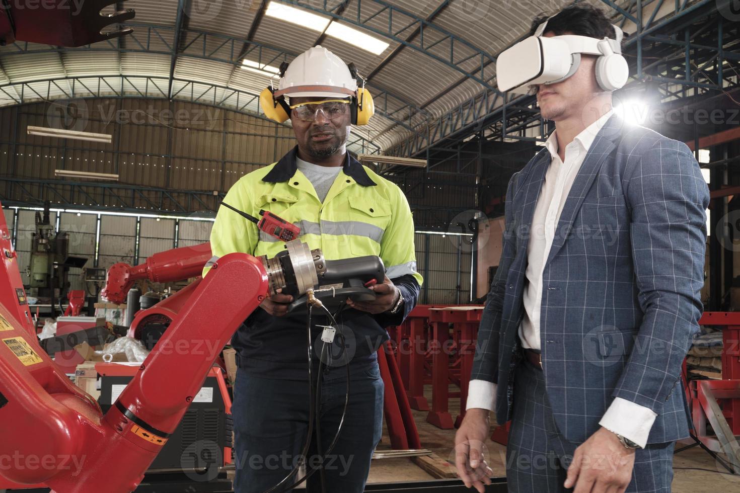 Der afroamerikanische Ingenieur demonstriert dem Kunden die Roboterarmsteuerung mit einem vr-Headset-Simulator in einer mechanischen Fertigungsfabrik, intelligenten Industriemaschinen und futuristischer Technologie. foto