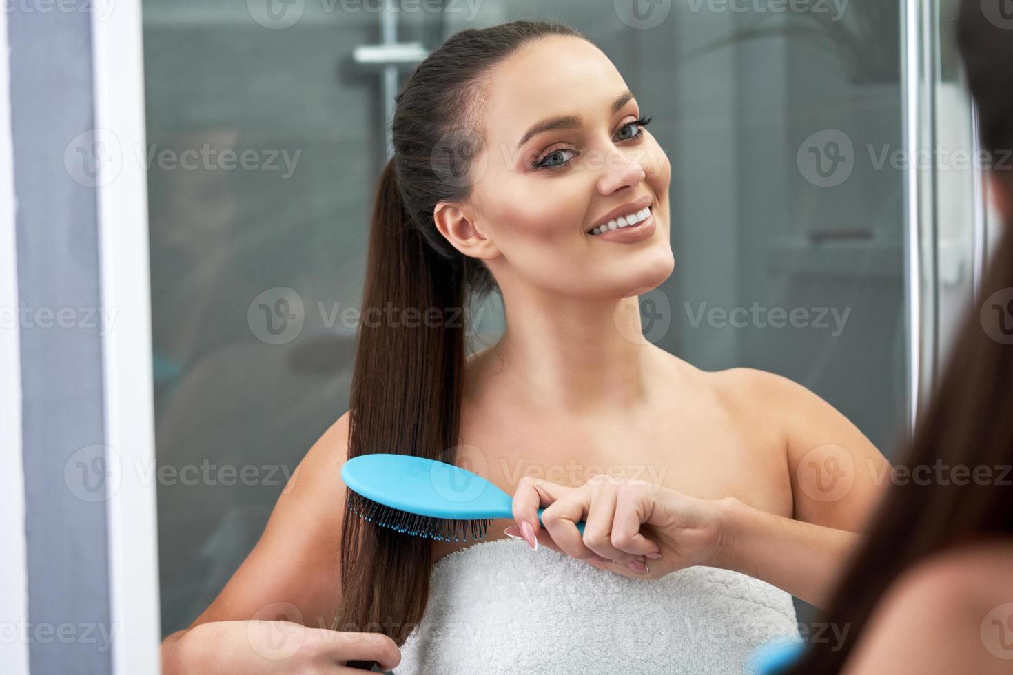 Frau, die Haare im Badezimmer nach Dusche bürstet foto