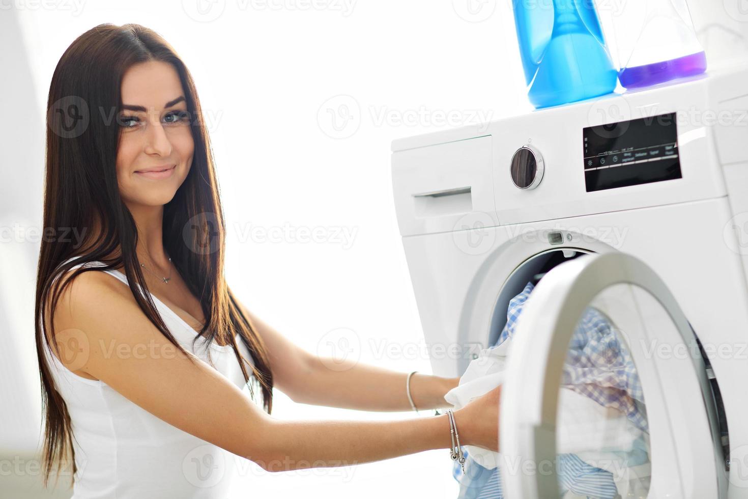 Porträt der jungen Hausfrau mit Wäsche neben der Waschmaschine foto