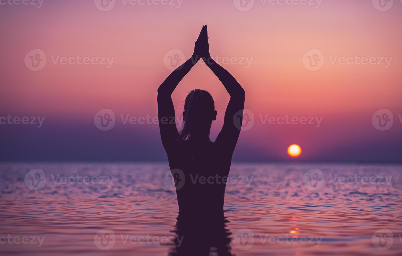 Silhouette einer jungen Frau, die bei Sonnenaufgang am Strand Yoga praktiziert foto