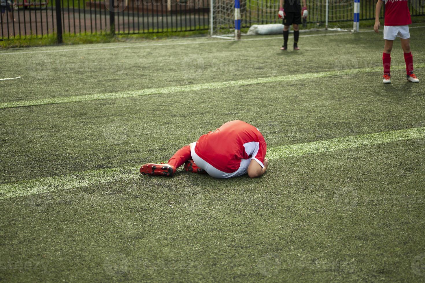 Fußballer fiel. Kind spielt Fußball. Verletzung auf dem Feld. Spieldetails. foto