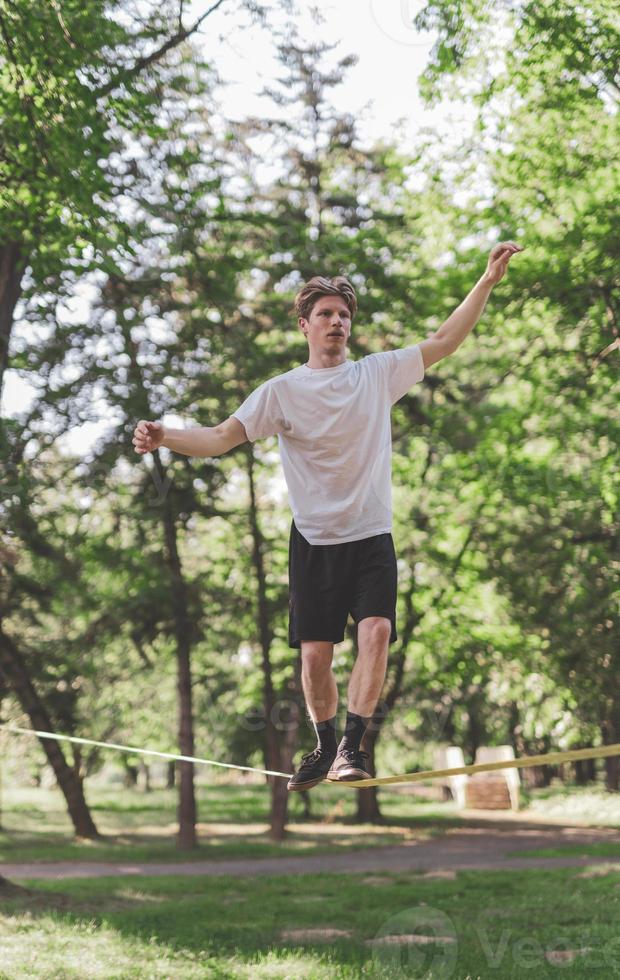 junger Mann balanciert und springt auf Slackline. Mann geht, springt und balanciert auf einem Seil im Park. foto