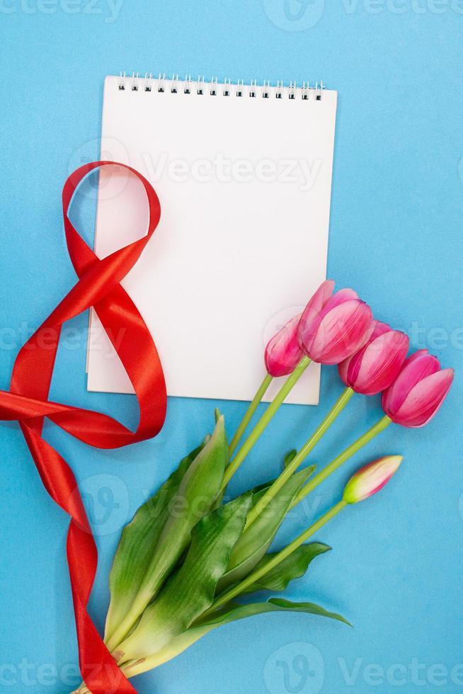 Nummer acht 8 aus rotem Band mit Strauß rosa Tulpen und Notizblock für Platz für Text auf blauem Hintergrund. feiertag, 8. märz, internationaler frauentag, geburtstag. Platz kopieren foto