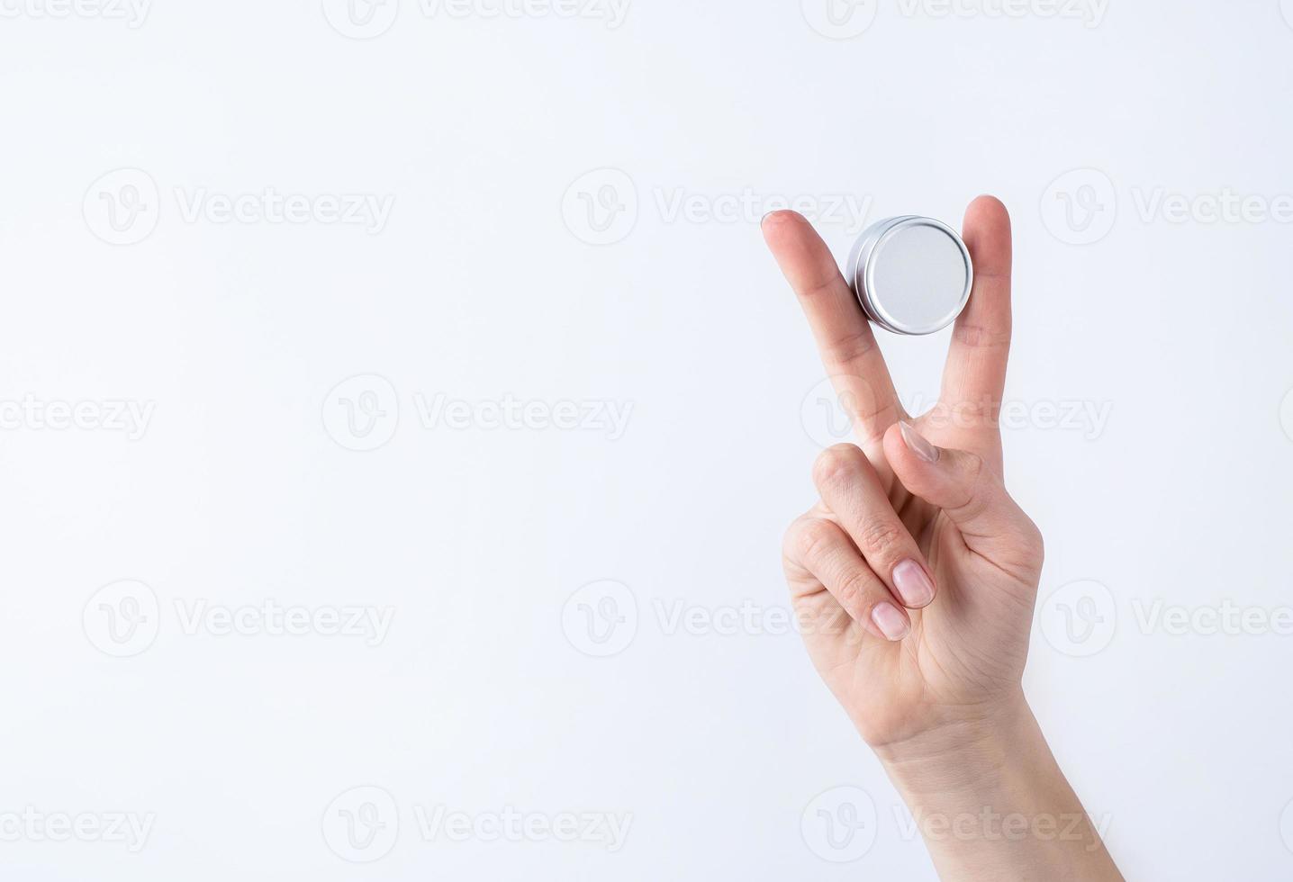 Frauenhand, die einen leeren runden Zinnbehälter für Lippenbalsam oder Creme auf hellgrauem Hintergrund hält foto