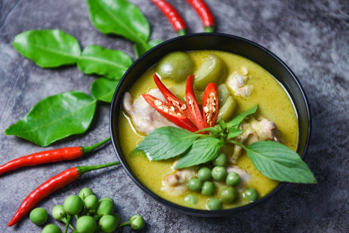 Grüne Curry-Hähnchen-Küche asiatisches Essen auf dem Tisch - thailändisches Essen Grünes Curry auf Suppenschüssel mit Zutat Kräutergemüse auf dunklem Plattenhintergrund foto