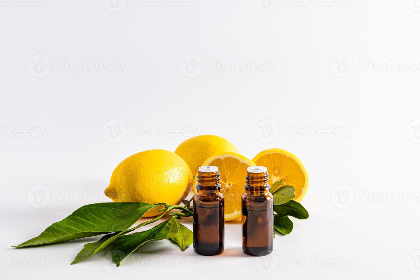 Vorderansicht von zwei medizinischen Flaschen mit ätherischem Zitronenöl gegenüber reifen Früchten. weißer Hintergrund. ein Blanko-Layout für die Produktpräsentation. foto