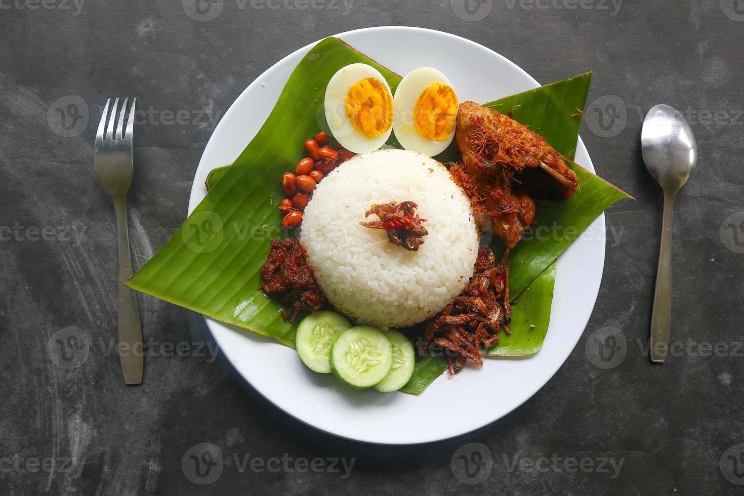 Nasi Lemak ist ein traditionelles malaiisches Gericht aus gekochten Eiern, Bohnen, Sardellen, Chilisauce und Gurken. aus einem Gericht, das auf einem Bananenblatt serviert wird foto