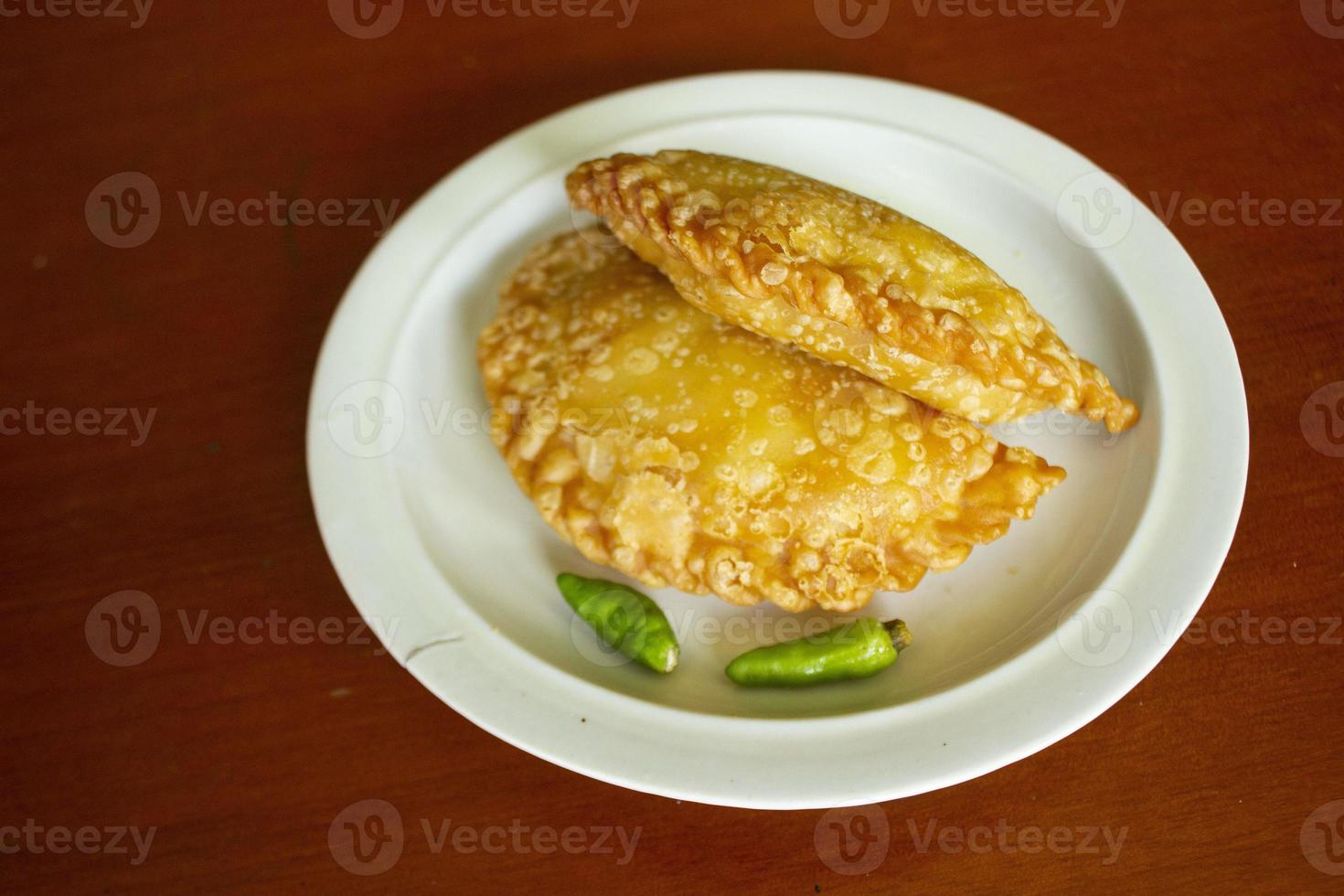 pastie kuchen oder gebäckkuchen oder kue pastell serviert mit grünem chili in einem kleinen teller auf holzhintergrund. indonesischer pastellkuchen foto