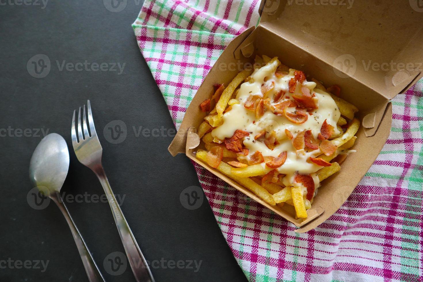 gebratene Pommes mit geschmolzenem Cheddar-Käse oder gebratenem Käse mit Wurstscheiben auf Schachtel foto