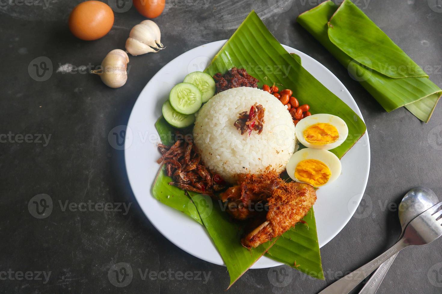 Nasi Lemak ist ein traditionelles malaiisches Gericht aus gekochten Eiern, Bohnen, Sardellen, Chilisauce und Gurken. aus einem Gericht, das auf einem Bananenblatt serviert wird foto