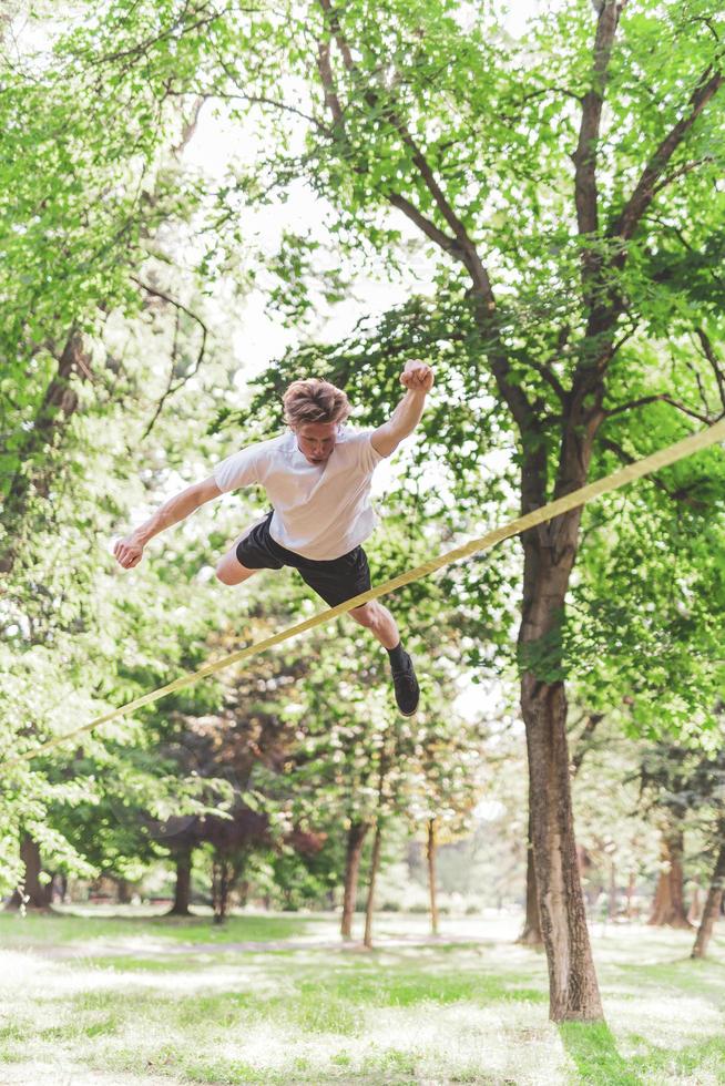 junger Mann balanciert und springt auf Slackline. Mann geht, springt und balanciert auf einem Seil im Park. foto