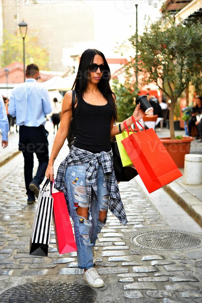 schöne frau, die mit einkaufstüten auf der straße geht. trendiges weibliches modell in der stadt, das einkaufstaschen hält. foto