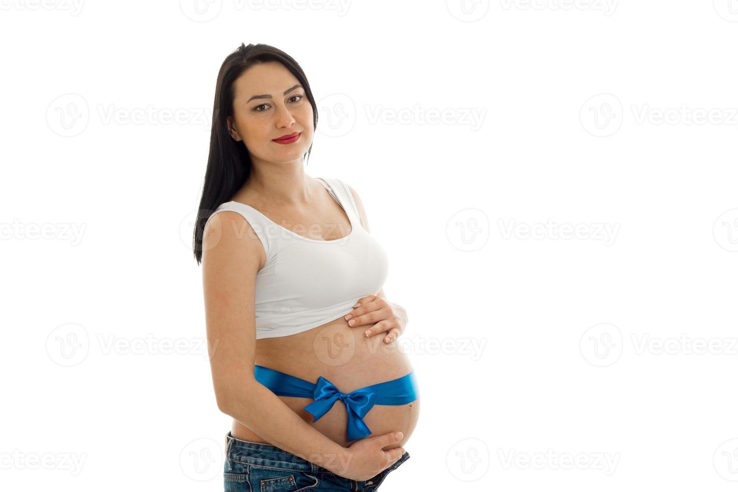 Junges schwangeres Mädchen mit dunklem Haar mit blauem Klebeband auf dem Bauch, das isoliert auf weißem Hintergrund in die Kamera schaut foto