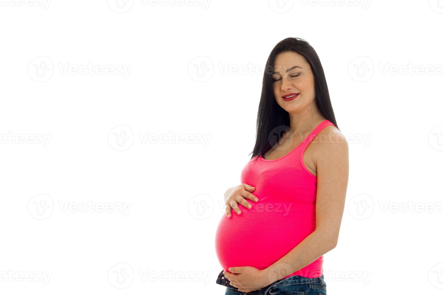 junge lächelnde schwangere frau in einem rosa t-shirt hält hände bauch foto