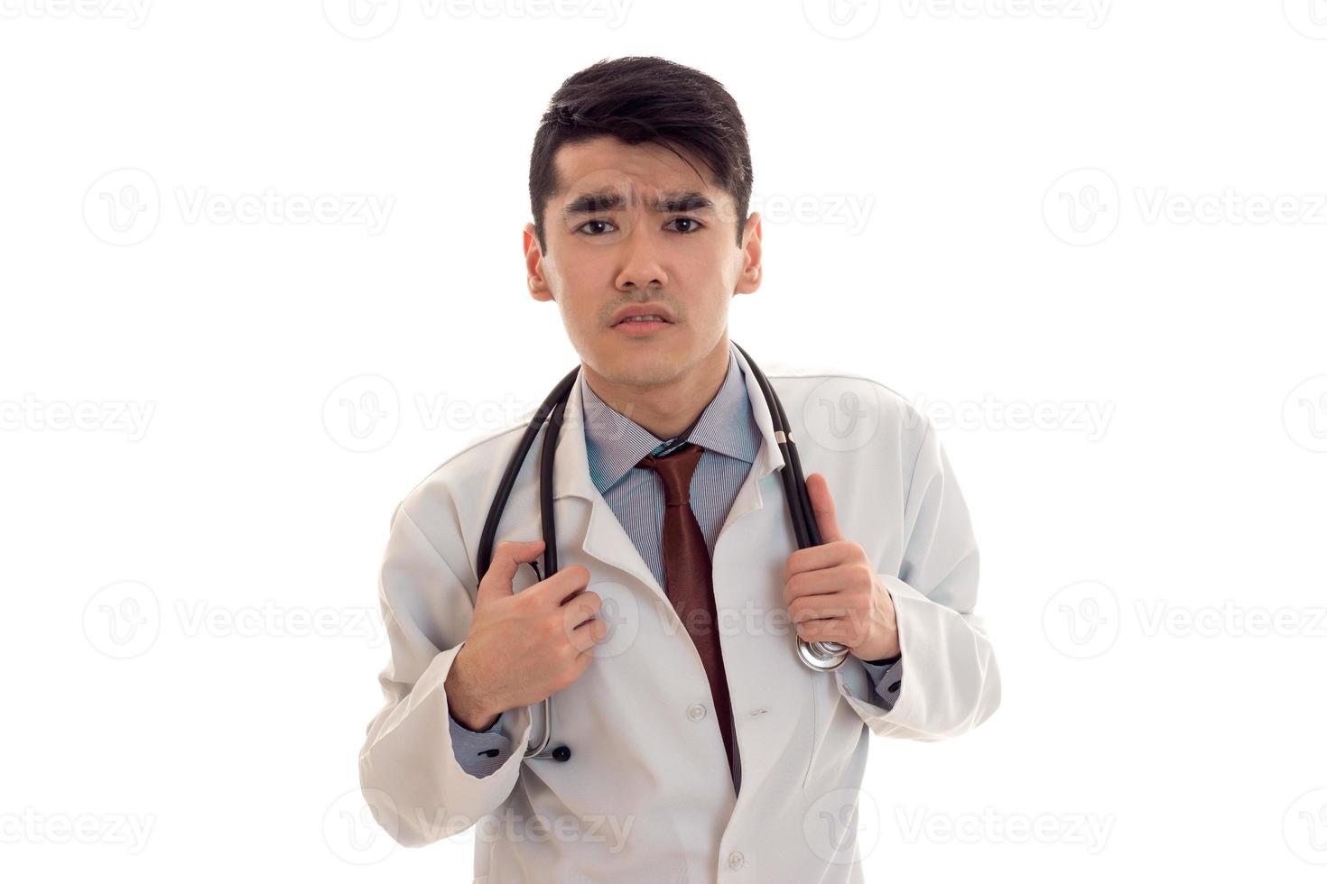 junger männlicher Arzt in Uniform mit Stethoskop, der isoliert auf weißem Hintergrund in die Kamera schaut foto
