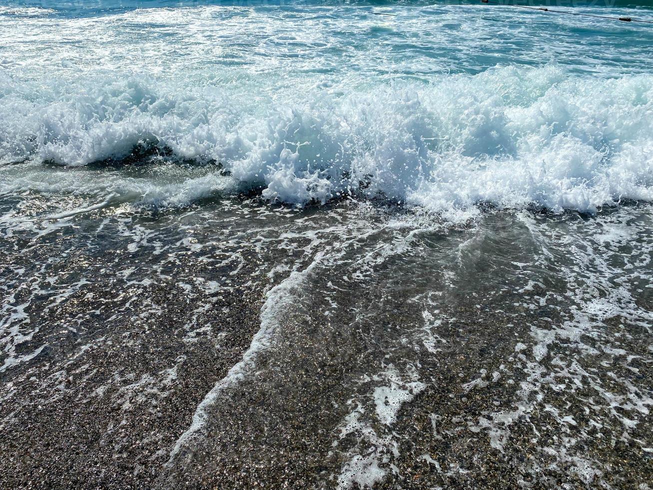 Wasserwellen im Meer und Sand mit kleinen natürlichen bunten Steinen an der Küste, kleine Kieselsteine am Strand. Hintergrund, Textur foto