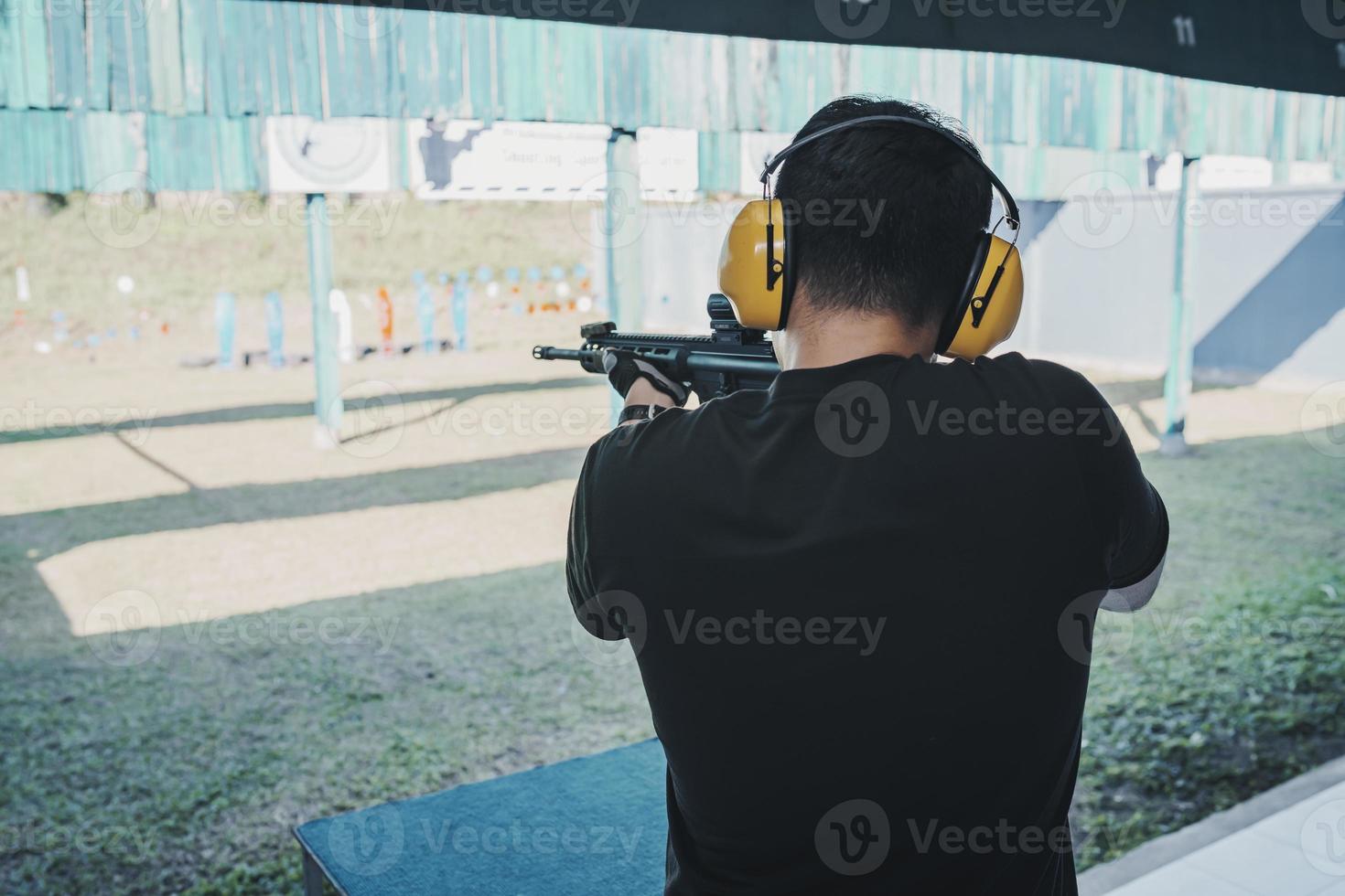 asiatischer schütze, der geräuschunterdrückende kopfhörer und schwarze kleidung trägt, die das schießen von gewehren auf dem schießstand üben. Schießsport zur Meditation und Selbstverteidigung, Freizeitaktivitäten. foto