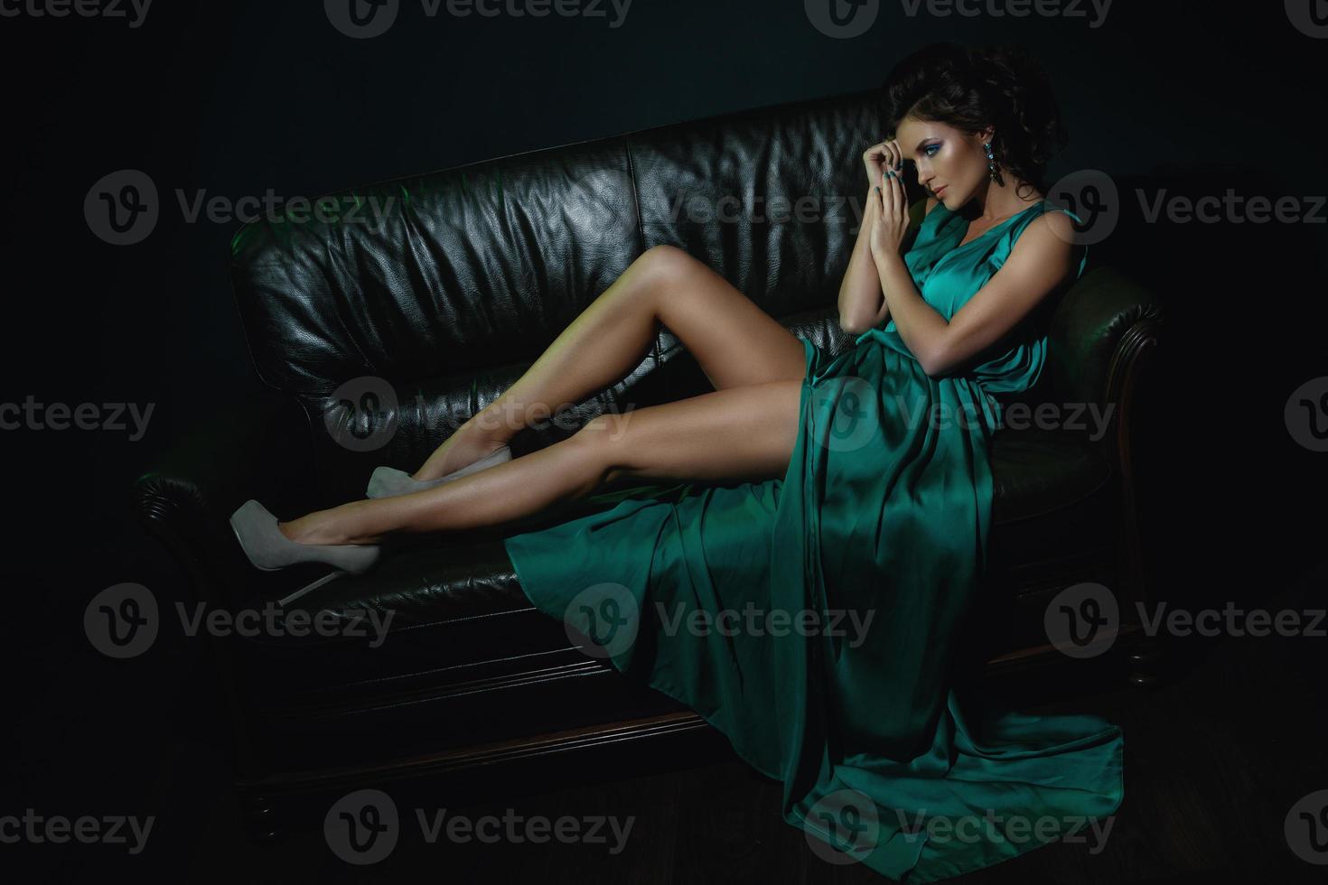 Model in schönem grünen Kleid posiert auf Ledercouch foto