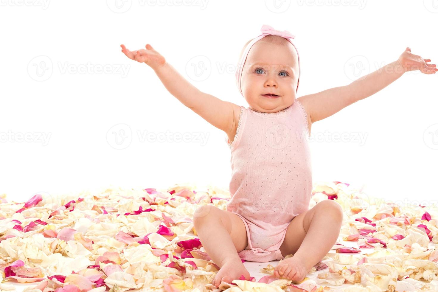 süßes Babymädchen sitzt umgeben von Rosenblättern foto