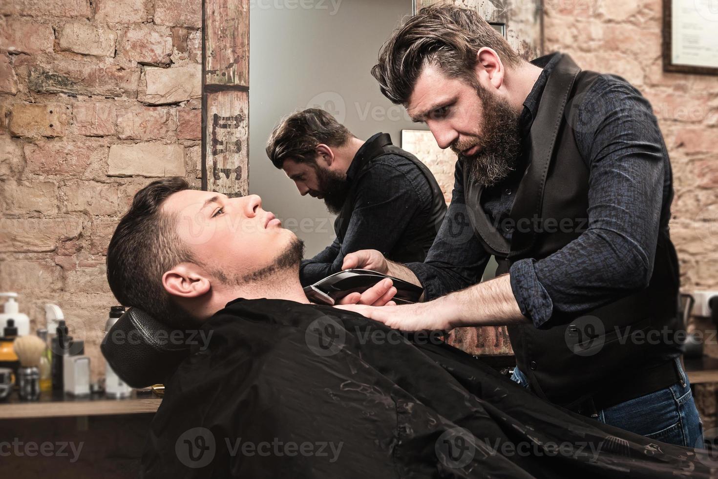 friseur, der bart mit einer haarschneidemaschine im salon rasiert foto