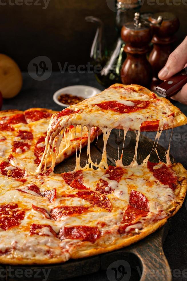 Peperoni-Pizza mit einer Scheibe, die mit Käse gezogen wurde foto