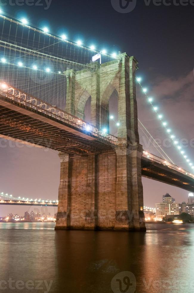 Brooklyn Bridge Nahaufnahme über East River in der Nacht in New York City Manhattan mit Lichtern und Reflexionen. foto