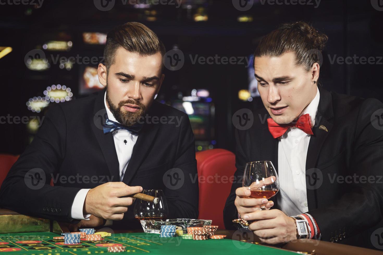 gutaussehende Typen, die Cognac trinken und im Casino Roulette spielen foto