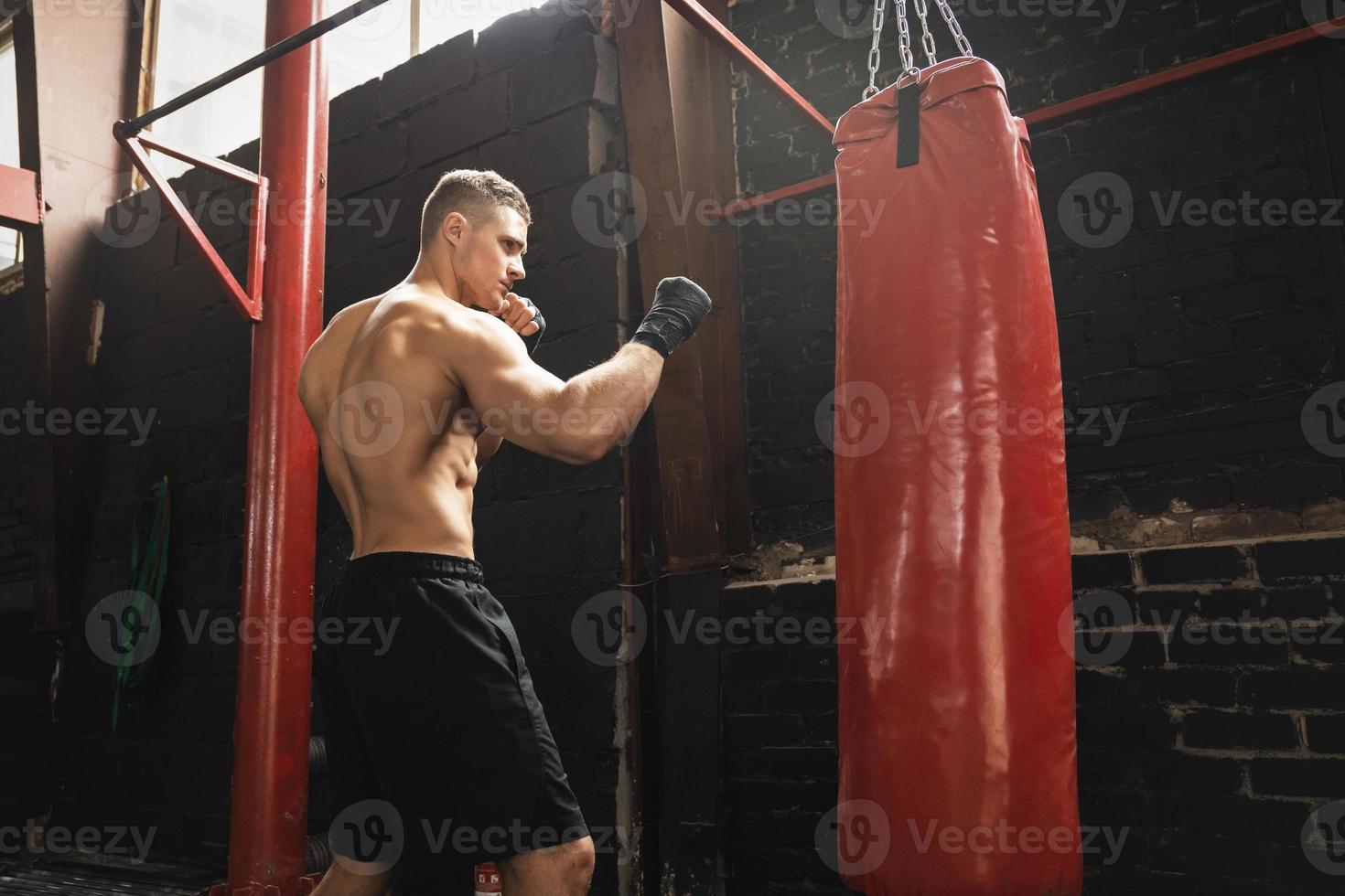 starker junger MMA-Kämpfer und roter Boxsack foto