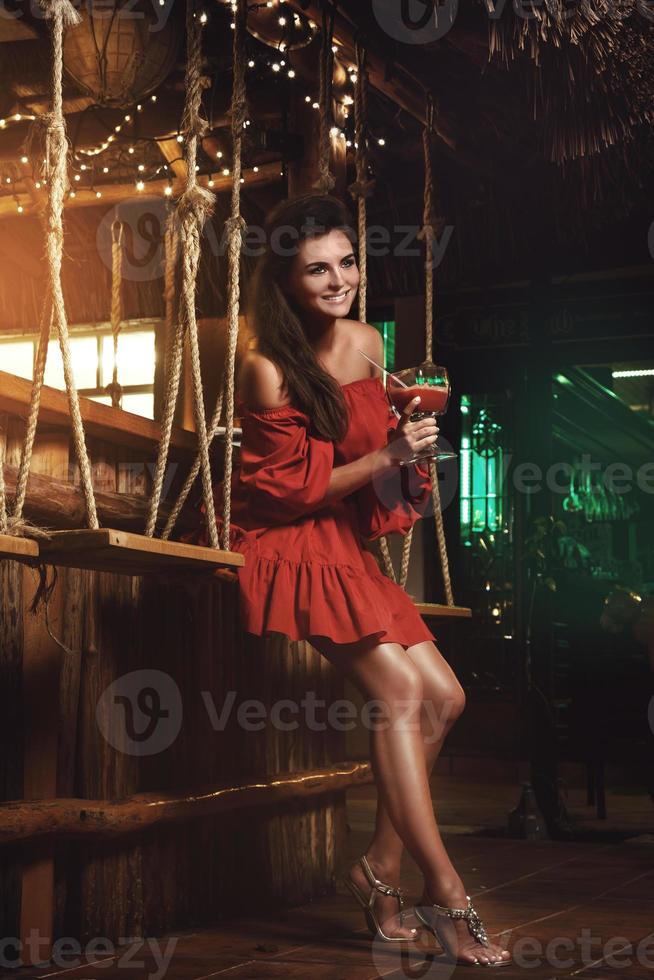 charmante Frau mit rotem Kleid in der Sommerbar am Abend foto