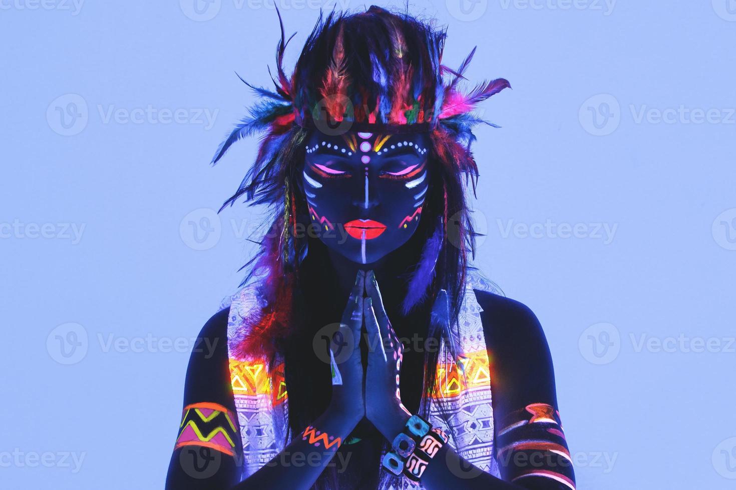 Modell im Bild des amerikanischen Ureinwohners mit Neon-Make-up, das aus fluoreszierender Farbe im ultravioletten Licht besteht. foto