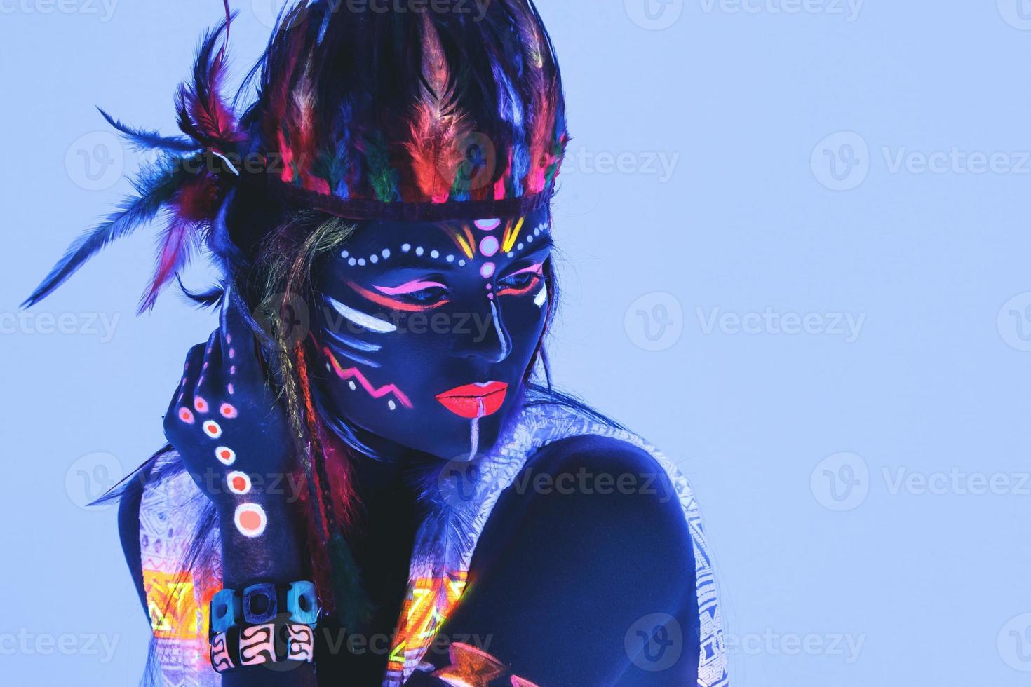 Modell im Bild des amerikanischen Ureinwohners mit Neon-Make-up, das aus fluoreszierender Farbe im ultravioletten Licht besteht. foto