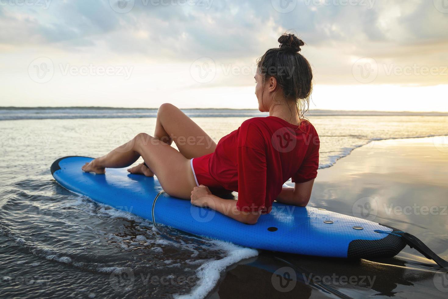 Frau, die nach ihrer Surfsession auf dem Surfbrett am Strand sitzt foto