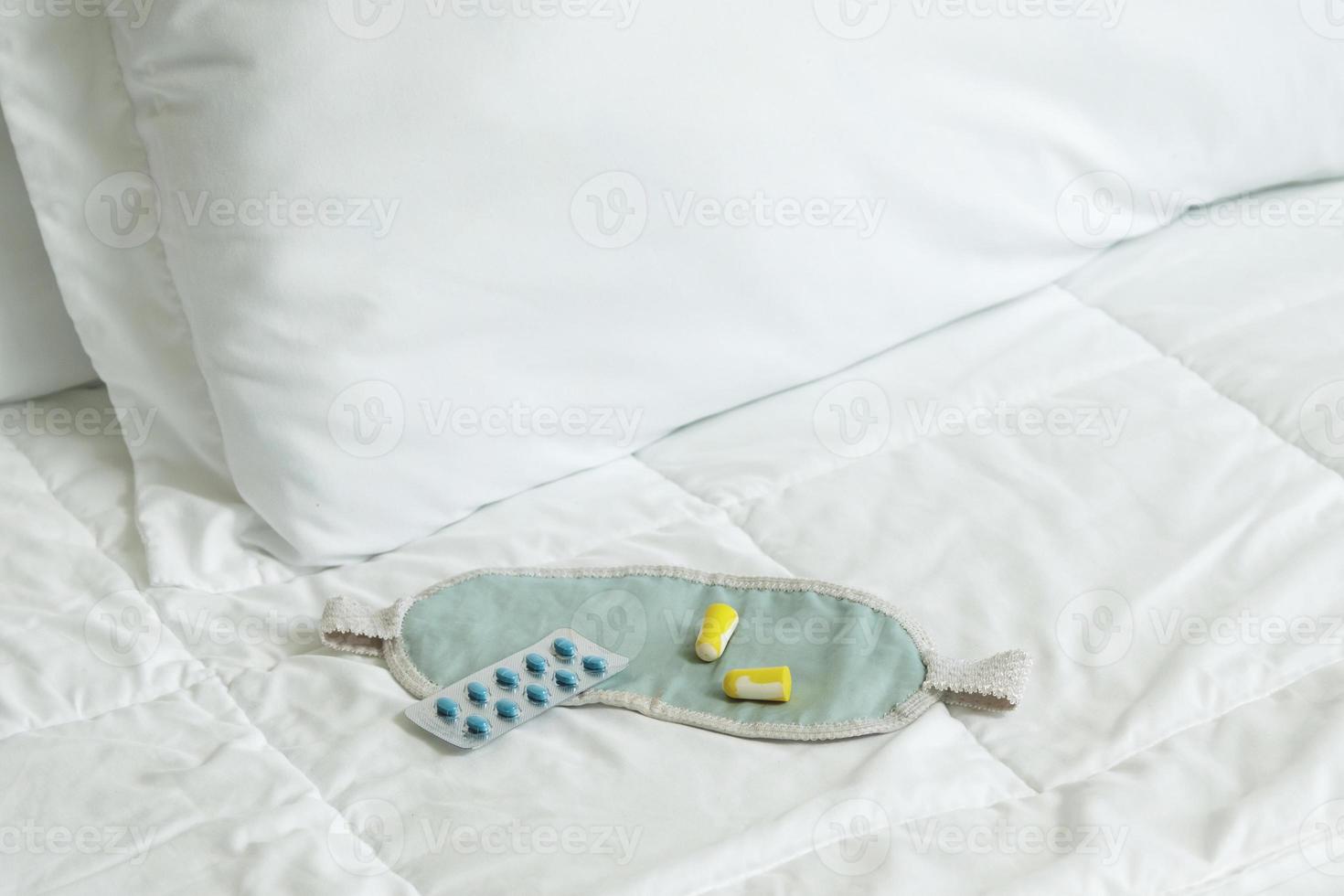 Ohrstöpsel, Augenbinde und Schlaftabletten auf dem Bett foto