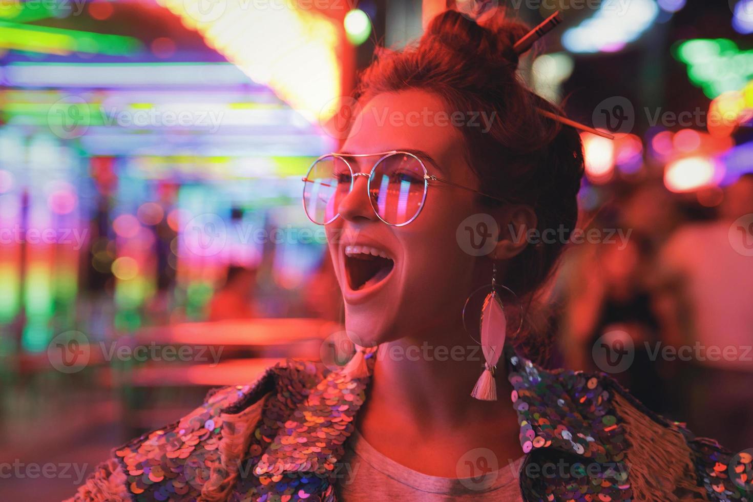 Frau mit funkelnder Jacke auf der Stadtstraße mit Neonlichtern foto