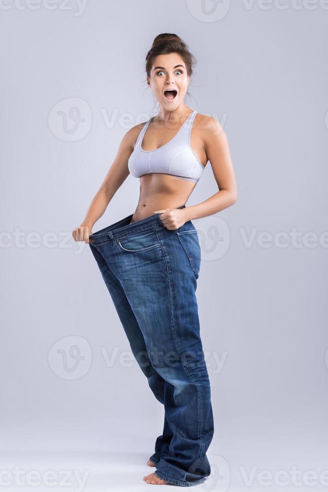 glückliche Frau in Jeans nach Gewichtsverlust auf grauem Hintergrund foto