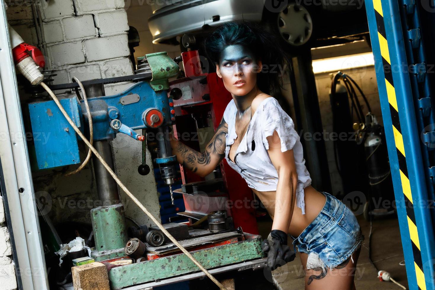 Mechanikerin in der Garage mit künstlerischem Make-up im Gesicht, stilisiert wie ein schmutziger Fleck foto