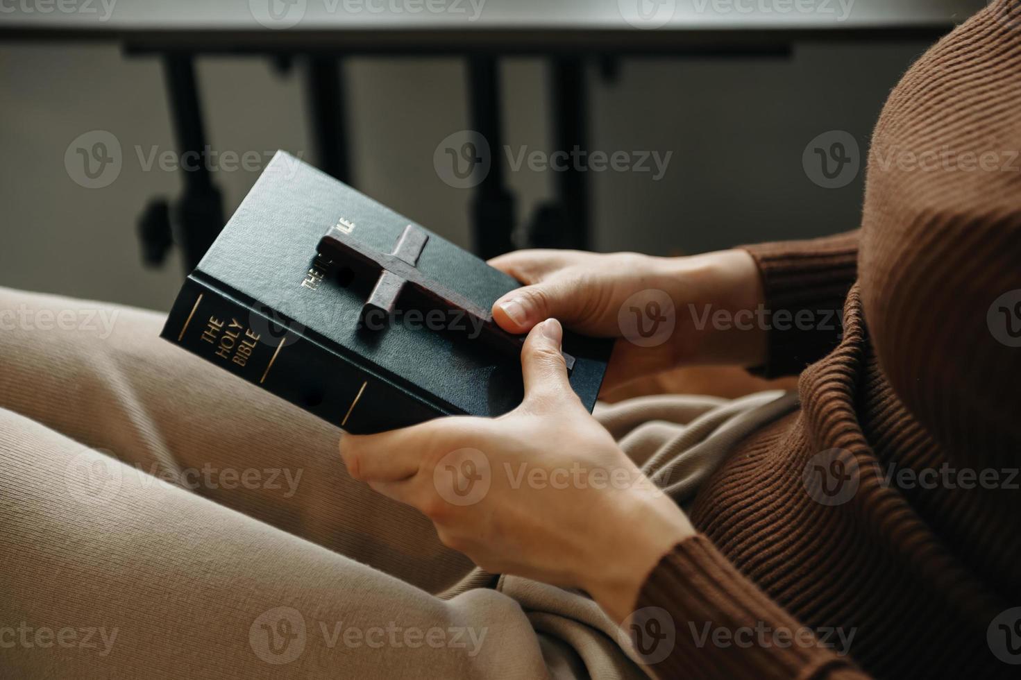 frau, die sitzt und die schriften studiert. das holzkreuz in den händen. christliche bildungskonzepte öffnen die heilige schrift foto