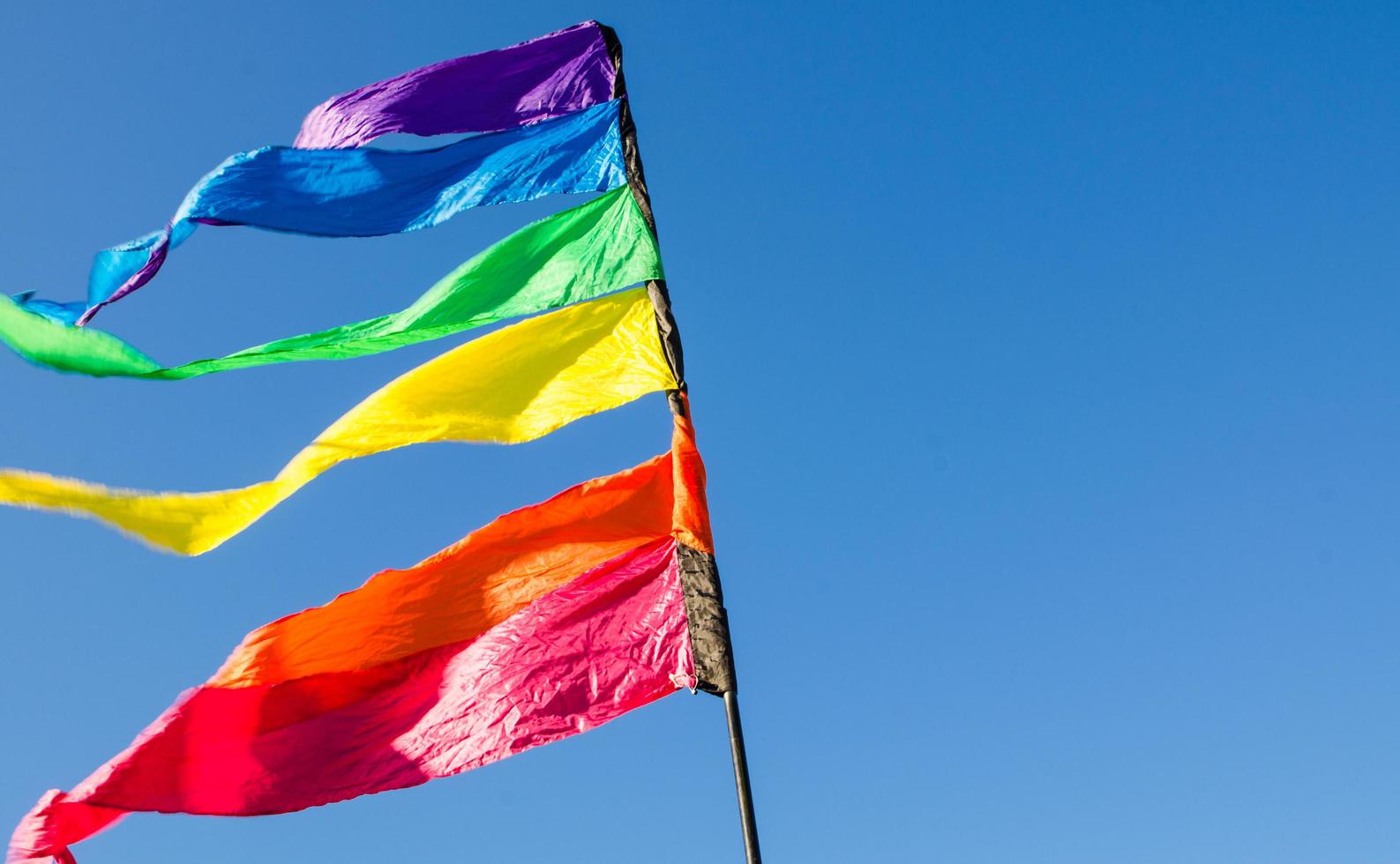 bunte Regenbogen-Dreieck-Flagge zeigt sich gegen den blauen Himmel. foto