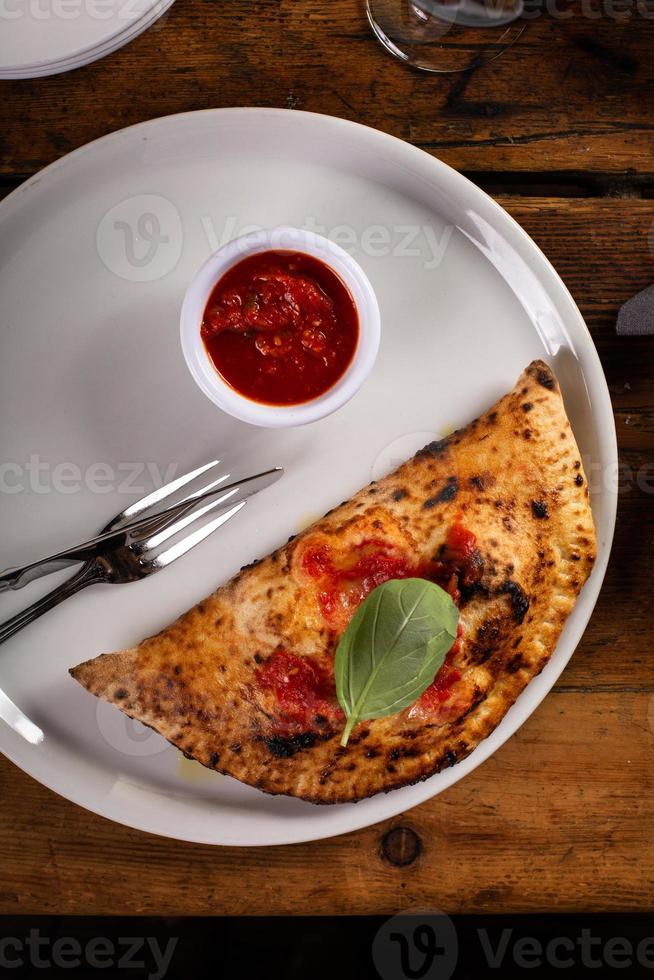 Italienische Calzone mit Marinara-Sauce ganz auf einem Teller foto