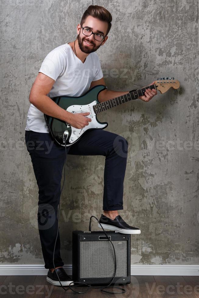 stylischer bärtiger kerl mit gitarre gegen betonwand foto