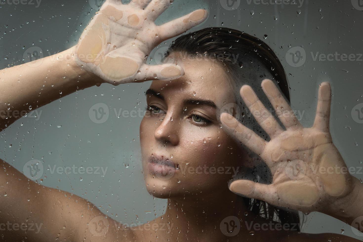 Porträt einer schönen Frau, die durch nasses Glas eingefangen wurde foto