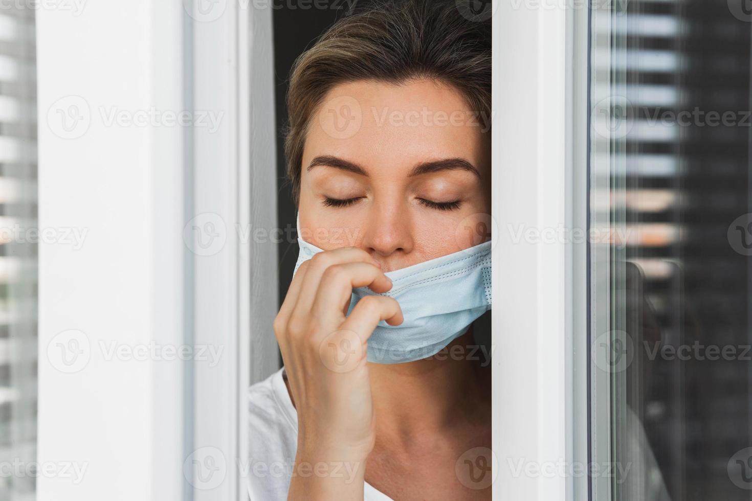 Frau geht auf einen Balkon, um tief Luft zu holen, weil sie eine Präventionsmaske benutzte foto